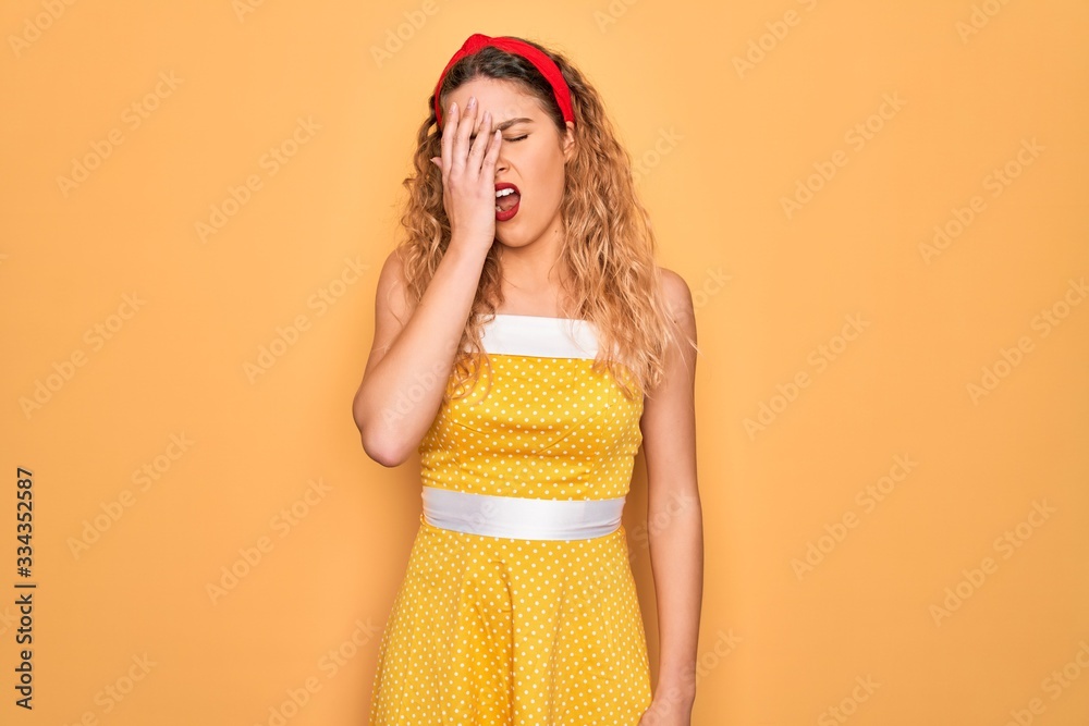 Beautiful blonde pin-up woman with blue eyes wearing diadem standing over yellow background Yawning tired covering half face, eye and mouth with hand. Face hurts in pain. Beautiful blonde pin-up woman with blue eyes wearing diadem standing over yellow background Yawning tired covering half face, eye and mouth with hand. Face hurts in pain.