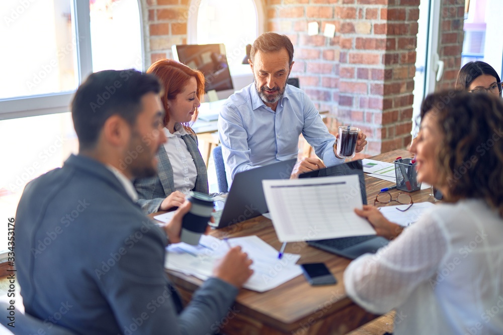 Group of business workers working together. Sitting on desk using laptop reading documents at the office Group of business workers working together. Sitting on desk using laptop reading documents at the office