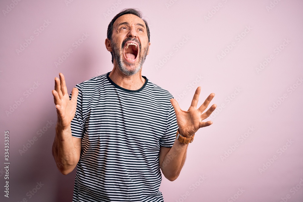 Middle age hoary man wearing casual striped t-shirt standing over isolated pink background crazy and mad shouting and yelling with aggressive expression and arms raised. Frustration concept. Middle age hoary man wearing casual striped t-shirt standing over isolated pink background crazy and mad shouting and yelling with aggressive expression and arms raised. Frustration concept.