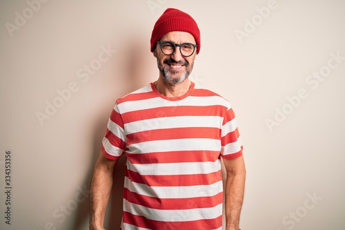 Middle age hoary man wearing striped t-shirt glasses and cap over isolated white background with a happy and cool smile on face. Lucky person.