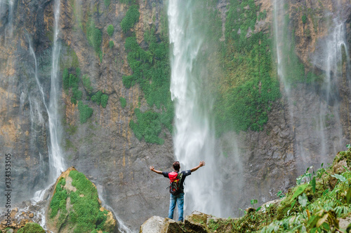 Happy man standing on the cliff to watch Tumpak Sewu waterfall scenic nature beauty.