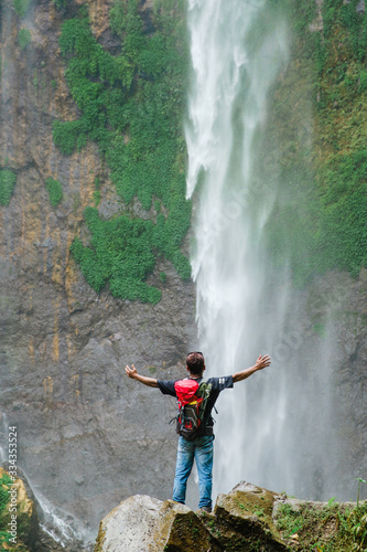 Happy man standing on the cliff to watch Tumpak Sewu waterfall scenic nature beauty.