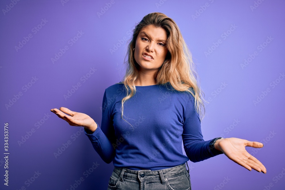 Young beautiful blonde woman wearing casual t-shirt over isolated purple background clueless and confused with open arms, no idea concept. Young beautiful blonde woman wearing casual t-shirt over isolated purple background clueless and confused with open arms, no idea concept.