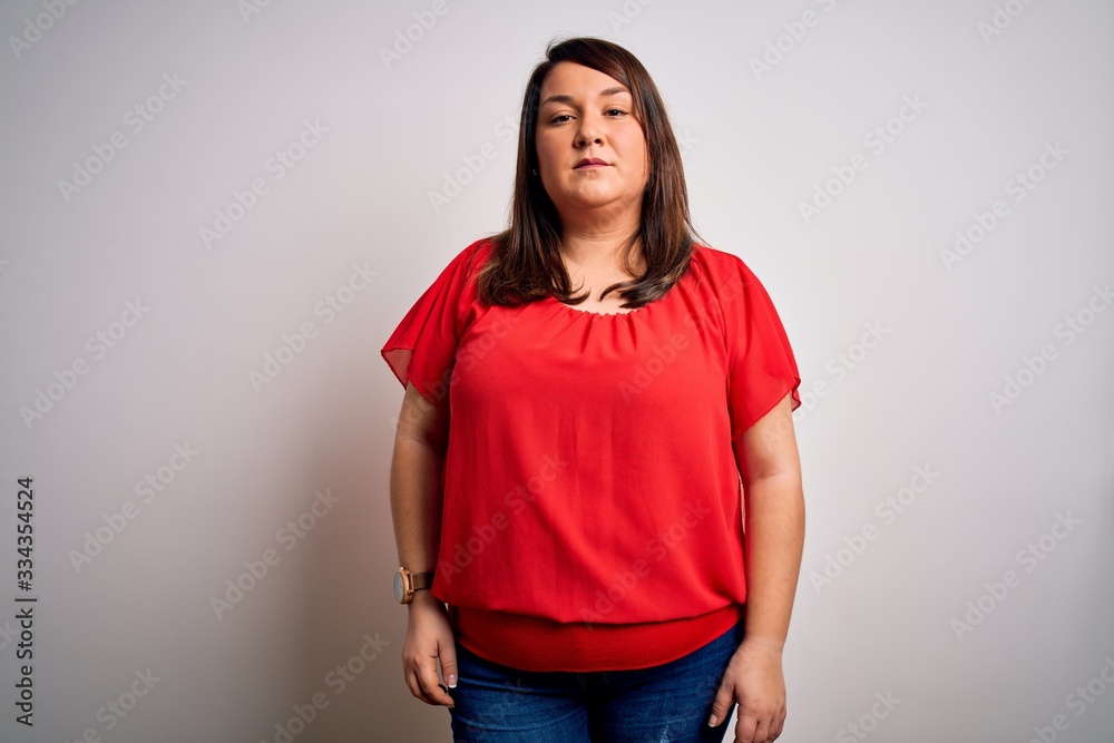 Beautiful brunette plus size woman wearing casual red t-shirt over isolated white background Relaxed with serious expression on face. Simple and natural looking at the camera.
