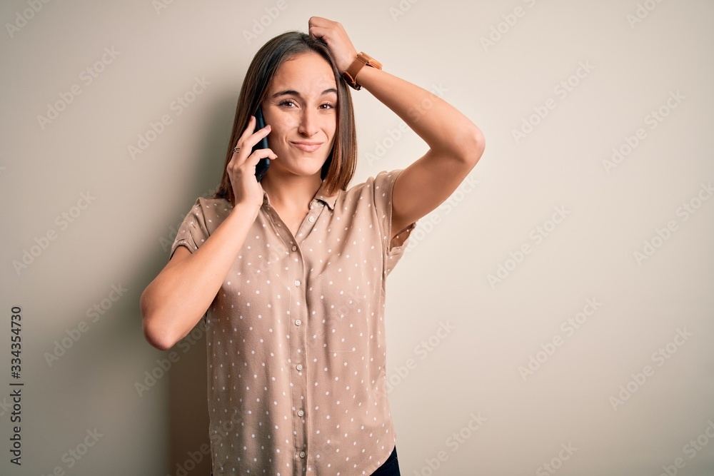 Young beautiful woman having conversation talking on the smartphone over white background confuse and wondering about question. Uncertain with doubt, thinking with hand on head. Pensive concept. Young beautiful woman having conversation talking on the smartphone over white background confuse and wondering about question. Uncertain with doubt, thinking with hand on head. Pensive concept.