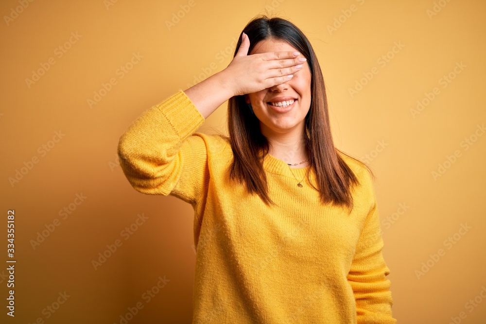 Young beautiful woman wearing casual sweater over yellow isolated background smiling and laughing with hand on face covering eyes for surprise. Blind concept. Young beautiful woman wearing casual sweater over yellow isolated background smiling and laughing with hand on face covering eyes for surprise. Blind concept.