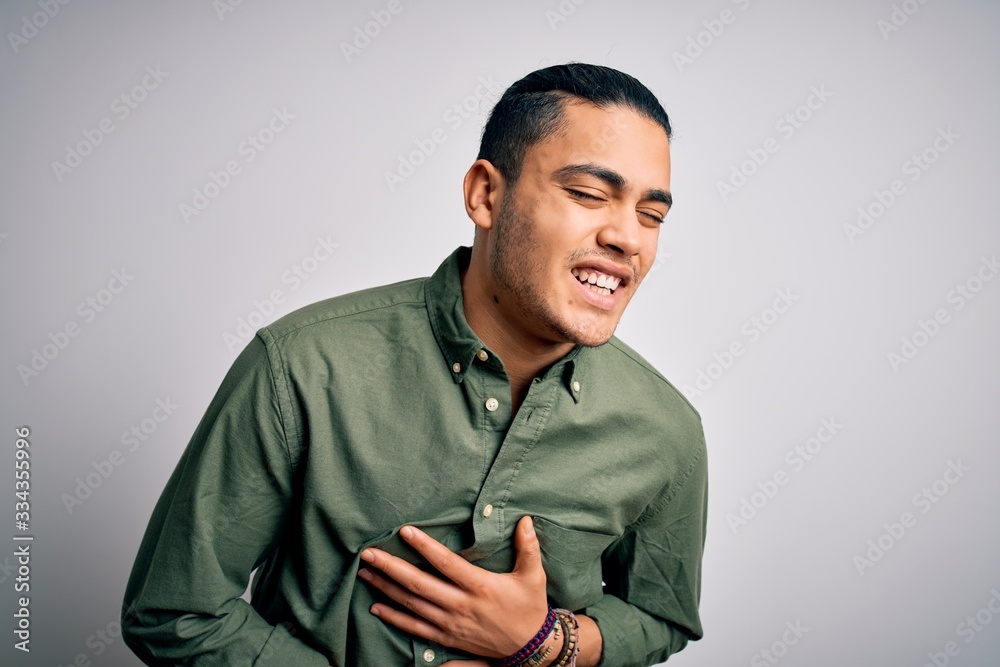Young brazilian man wearing casual shirt standing over isolated white background with hand on stomach because nausea, painful disease feeling unwell. Ache concept. Young brazilian man wearing casual shirt standing over isolated white background with hand on stomach because nausea, painful disease feeling unwell. Ache concept.