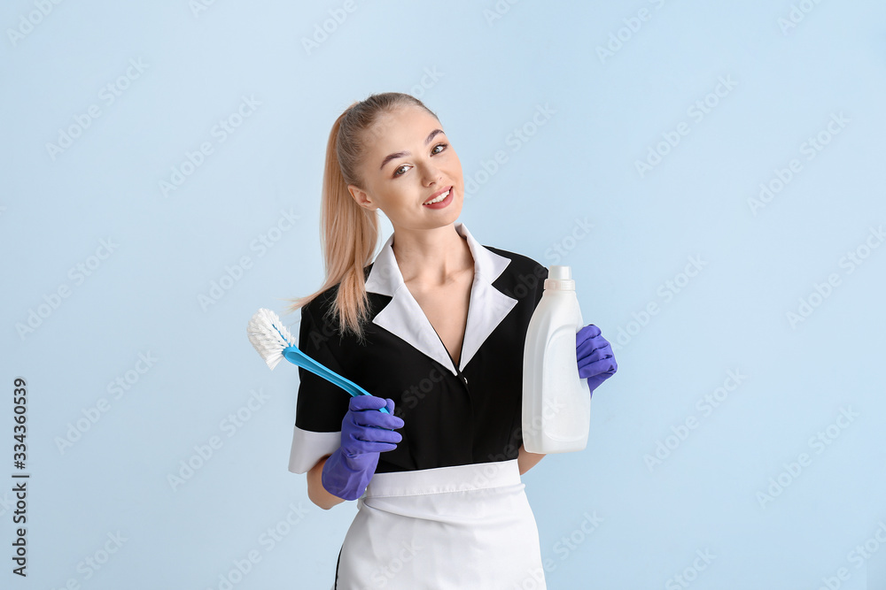 Beautiful young chambermaid with cleaning supplies on color background Beautiful young chambermaid with cleaning supplies on color background