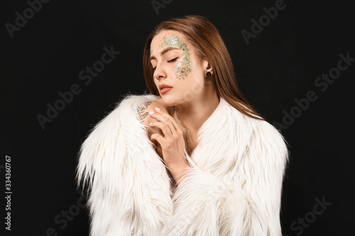 Fashionable young woman with glitters on her body against dark background
