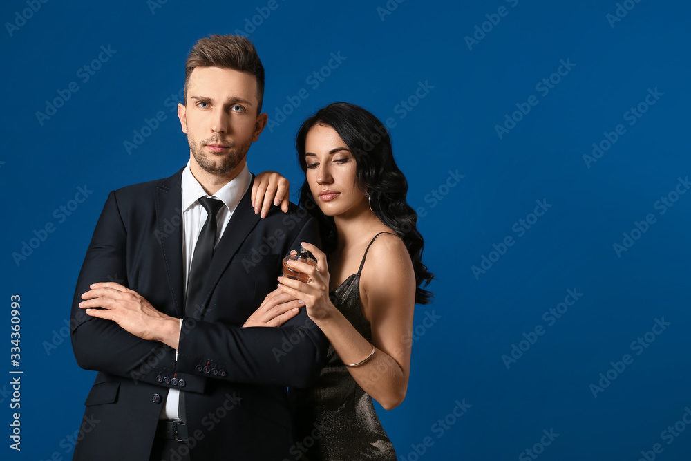 Stylish young couple with perfume on color background
