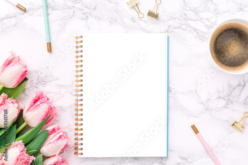 Pink tulips with festive stationary and coffee on white marble background. Feminine job, gender equality, home office and career concept. Isolated white copy space on the paper. Top view. Horizontal