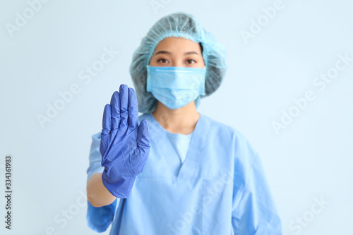 Asian doctor showing stop gesture on color background. Concept of epidemic