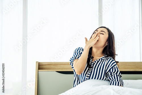 rest, holidays, comfort and people concept, Portrait of sleepy asian woman in sleepwear yawning after her waking up so early in the morning, Sitting on bed .