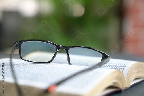 Reading glasses on top of an open book. Garden or green nature background.