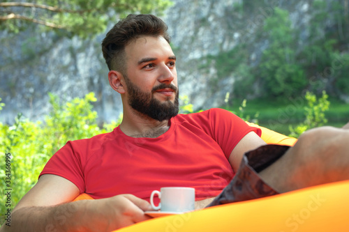 Close up portrait of handsome young bearded man relaxing outdoors drinking morning coffee. Tourism, taste of paradise