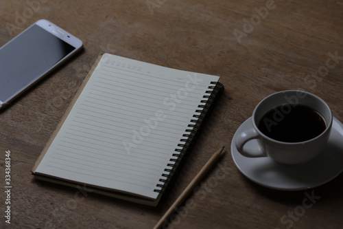 Notebook, white coffee cup and pencil on wooden table. Selective focus.
