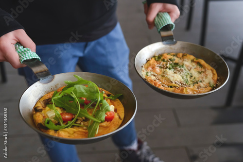 Man holds two pans of English breakfast - fried egg, beans, tomatoes, mushrooms, seeds served in a pan.