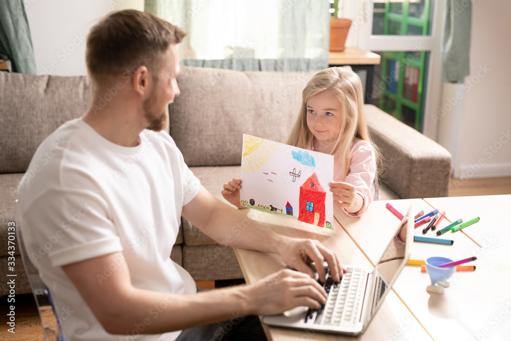 Cute smiling little daughter showing picture drawn with color pencils to her dad