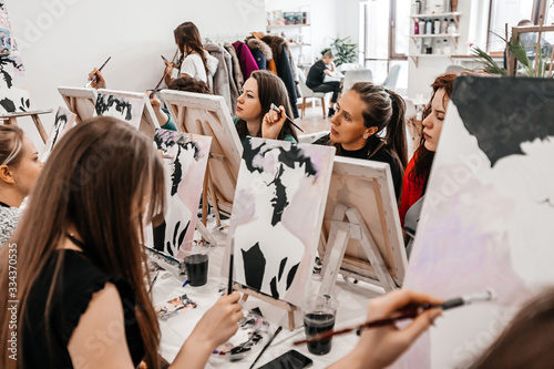 Young women paint with brushes on easels in art class. art school, creativity and people concept