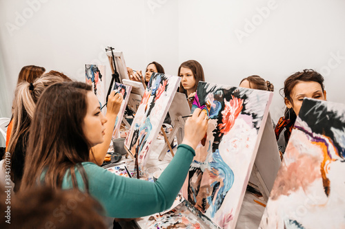 Young women paint with brushes on easels in art class. art school, creativity and people concept