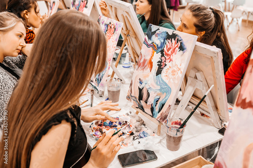 Young women paint with brushes on easels in art class. art school, creativity and people concept