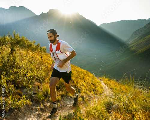A trail runner at sunrise, running up a mountain trail above a valley in the mountains