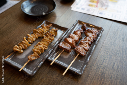 Chicken skin and beef skewers grilled on a black plate on a wooden table Is a Japanese yakitori menu Most popular with alcoholic drinks.