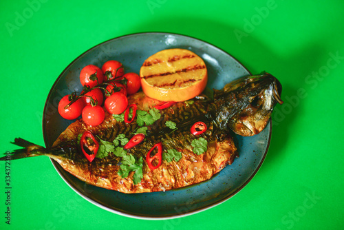 Fried fish with fresh herbs and lemon served on a blue plate over btight green background. photo