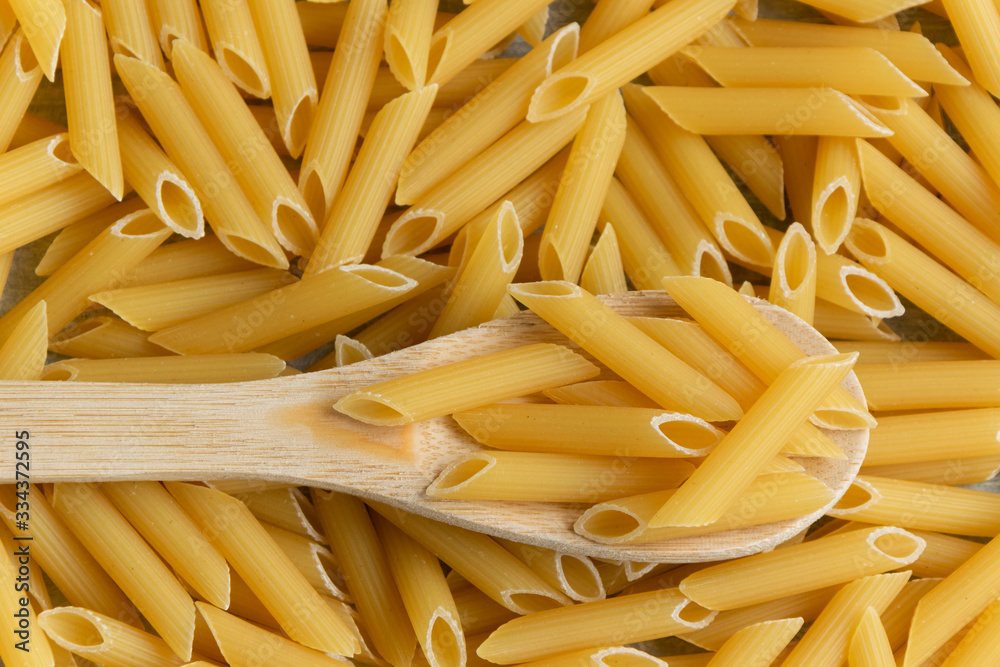 Food background - dry penne pasta and wooden spoon, whole wheat uncooked ingredient Food background - dry penne pasta and wooden spoon, whole wheat uncooked ingredient