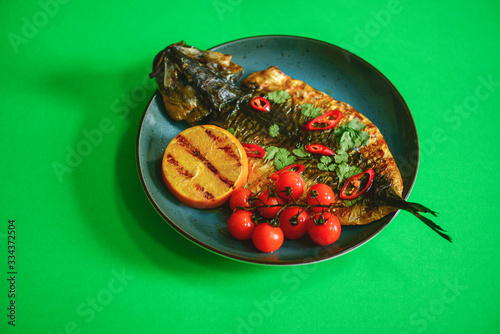 Fried fish with fresh herbs and lemon served on a blue plate over btight green background. photo