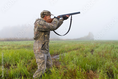a man takes aim with a rifle in a meadow on a foggy morning