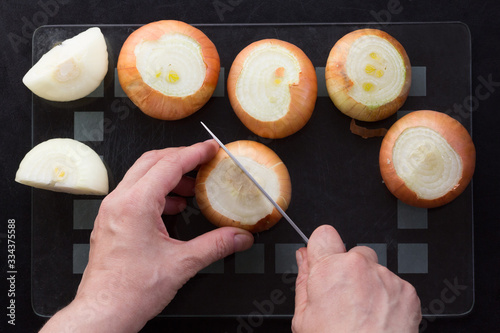 Top view of woman hands cutting in half unpeeled onion on the black background photo