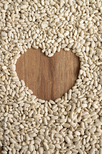 White raw aw beans background with wooden heart shape for space for text. Natural protein legume food