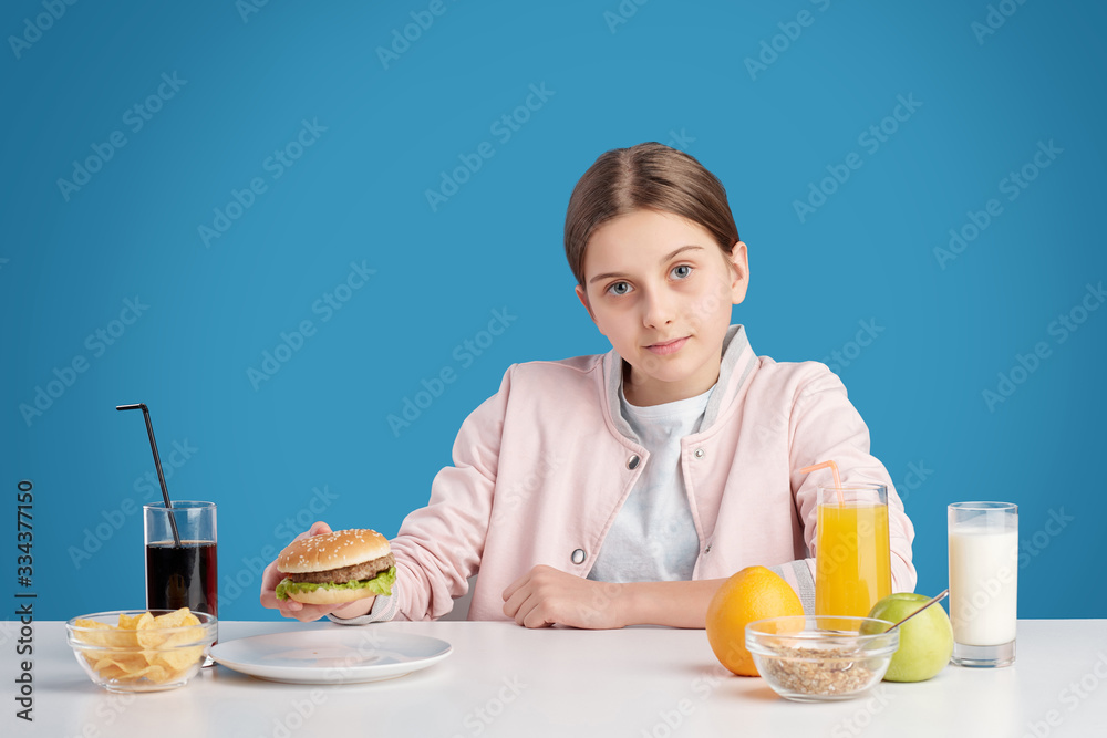 Pretty teenage girl looking at you while going to eat hamburger and potato chips Pretty teenage girl looking at you while going to eat hamburger and potato chips