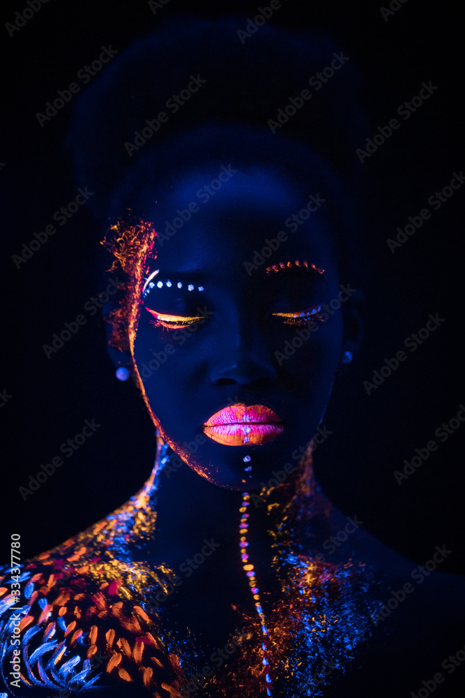 portrait of young fashion model woman in neon light. beautiful african model girl with colorful bright fluorescent makeup isolated on black. body-paint portrait of young fashion model woman in neon light. beautiful african model girl with colorful bright fluorescent makeup isolated on black. body-paint