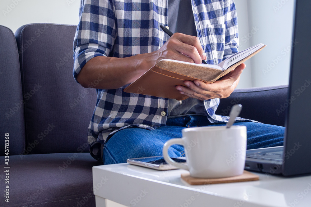 A man working or study online in the living room on the sofa. due to the spread of the virus Covid-19. Stay home, stop the spread the virus. stay safe, working from home and Social distance. A man working or study online in the living room on the sofa. due to the spread of the virus Covid-19. Stay home, stop the spread the virus. stay safe, working from home and Social distance.
