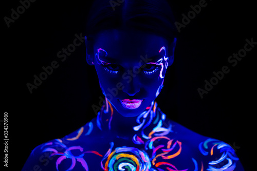 serious caucasian woman with fluorescent prints on skin, attractive model confidently look at camera, posing. colorful lines looks unusual, beautiful. isolated dark background photo