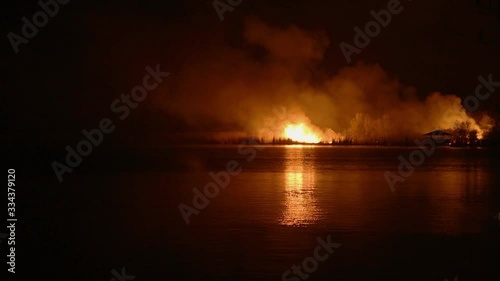Night forest fire, reflected on the water surface of the river