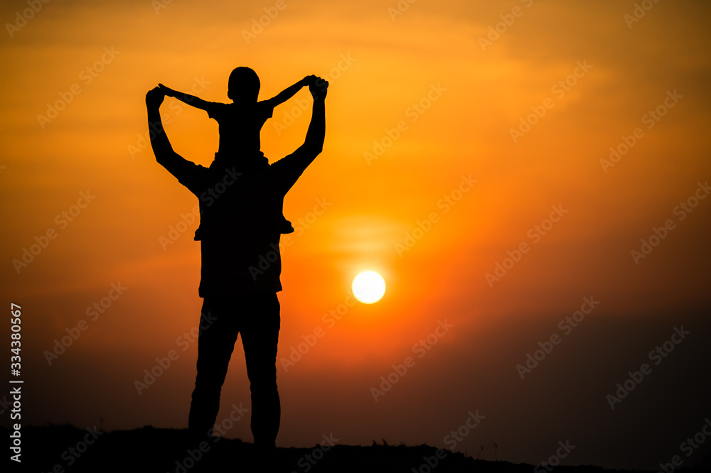 Fototapeta premium silhouette of a family with a boy riding his father's neck happily against the sunset sky