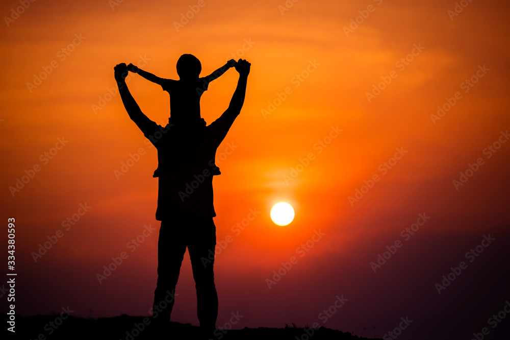 Fototapeta premium silhouette of a family with a boy riding his father's neck happily against the sunset sky