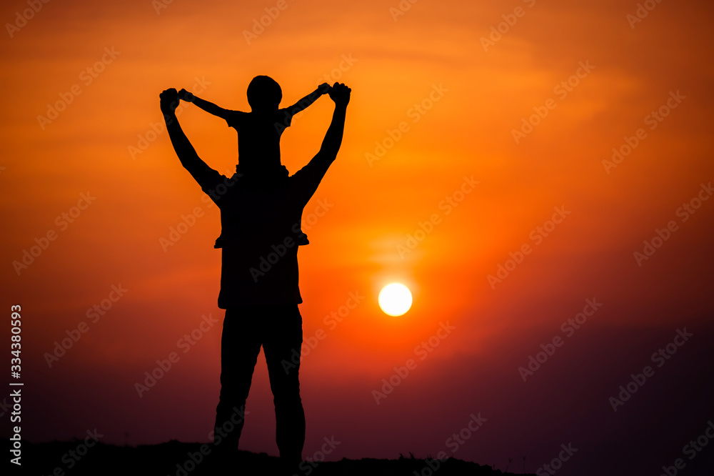 silhouette of a family with a boy riding his father's neck happily against the sunset sky