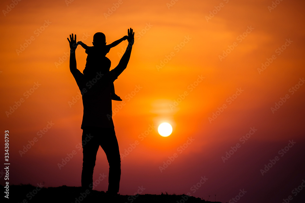 Fototapeta premium silhouette of a family with a boy riding his father's neck happily against the sunset sky