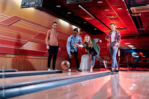 Foto Pretty young female throwing bowling ball on track during play with friends