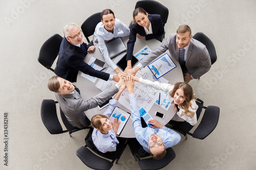 corporate, people and teamwork concept - happy business team sitting at table stacking hands