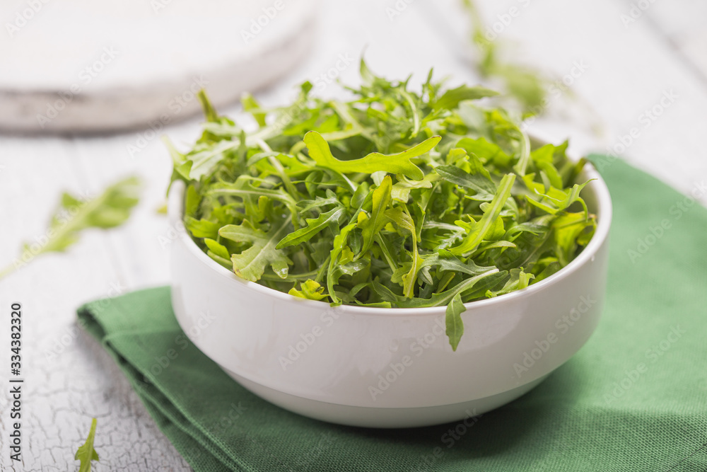 Fresh green arugula leaves on white bowl, rucola rocket salad on wooden rustic background with place for text. Selective focus, healthy food, diet. Nutrition concept Fresh green arugula leaves on white bowl, rucola rocket salad on wooden rustic background with place for text. Selective focus, healthy food, diet. Nutrition concept