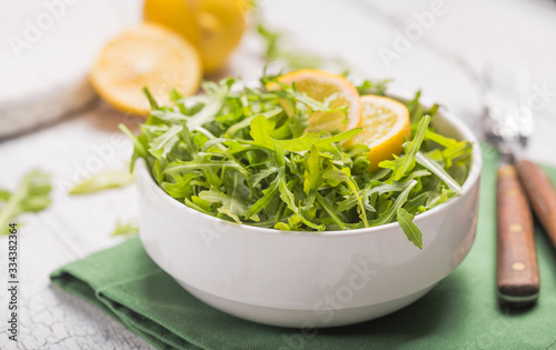 Fresh green arugula leaves on white bowl, rucola rocket salad on wooden rustic background with place for text. Selective focus, healthy food, diet. Nutrition concept