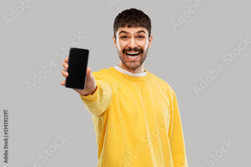 technology, communication and people concept - happy smiling young man showing smartphone over grey background