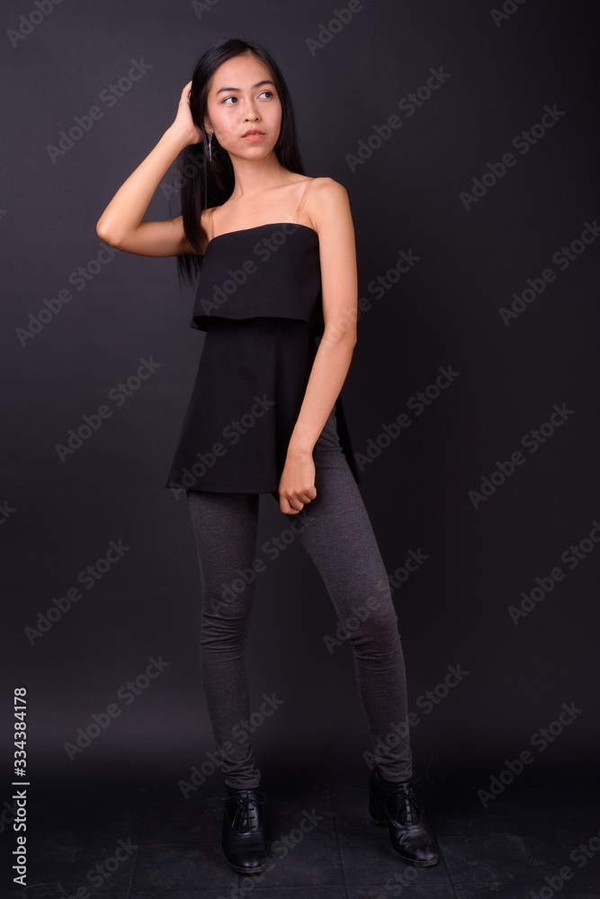 Full body shot of young beautiful Asian woman thinking Full body shot of young beautiful Asian woman thinking