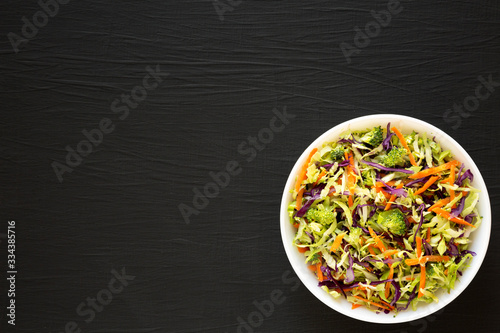 Homemade Raw Shredded Broccoli Slaw in a white bowl on a black background, top view. Flat lay, overhead, from above. Copy space.