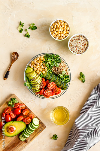 Veggie bowl. Vegetable salad with quinoa, avocado, tomato, spinach and chickpeas - on beige table. Top view